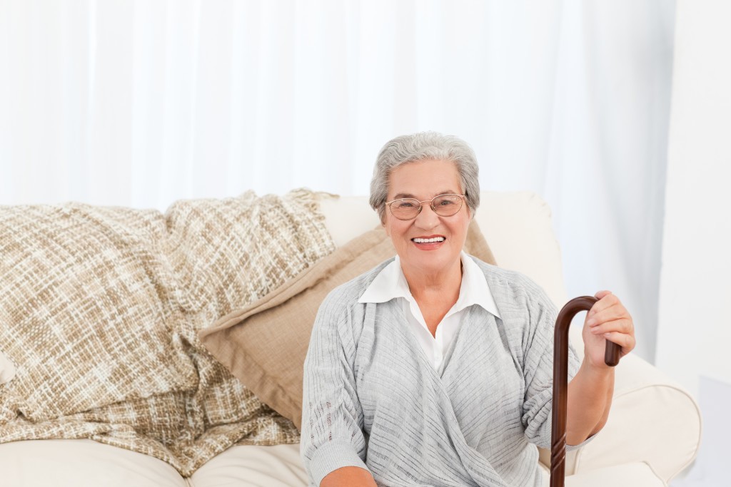 Mature woman sitting on the sofa with her walking stick at home