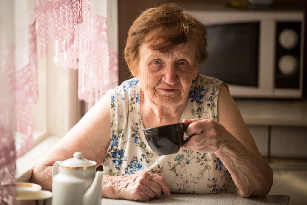 Old woman is drinking tea in his rural home