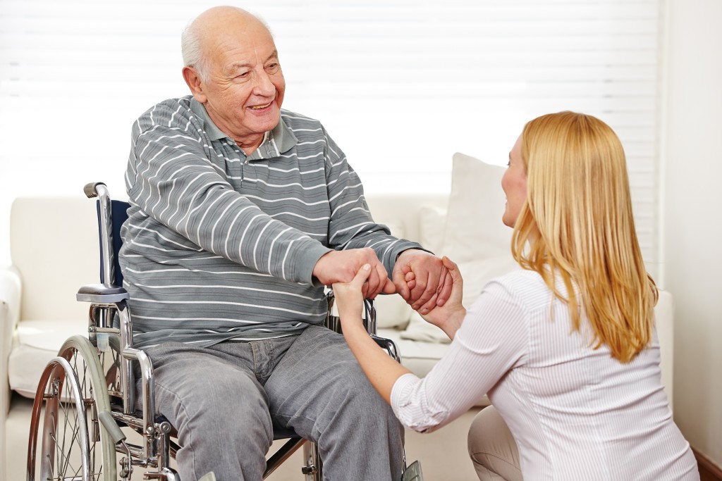 Woman holding hands of old man in wheelchair in a nursing home Woman holding hands of old man in wheelchair in a nursing home